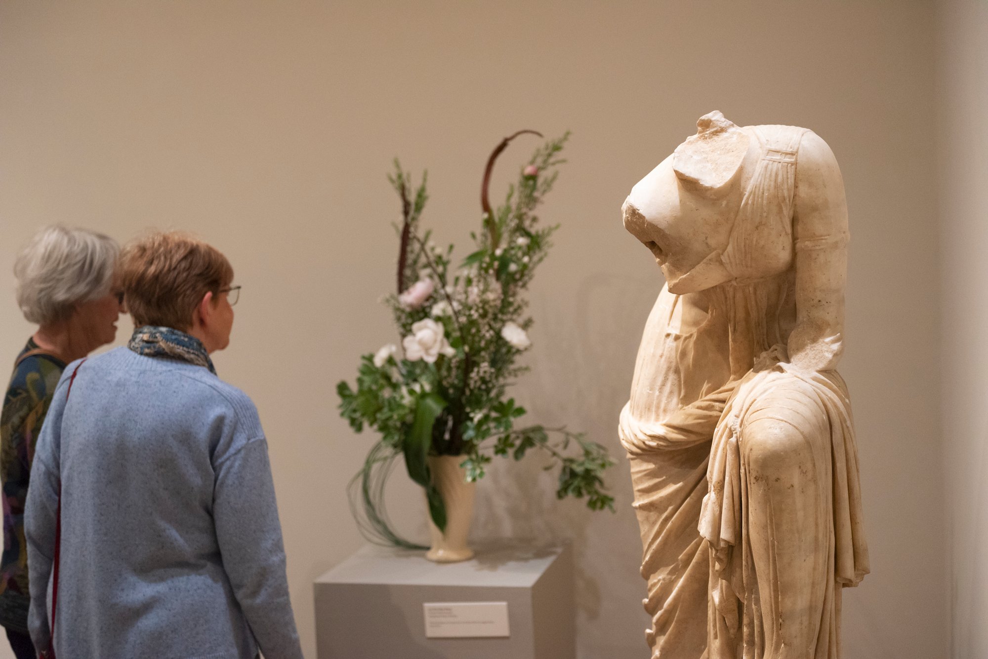 Two women look at a marble sculpture and a floral arrangement interpretation
