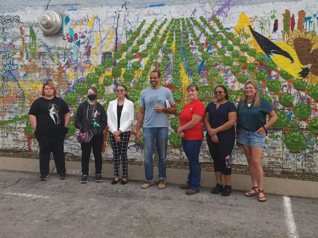 A group of adults pose in front of a mural.