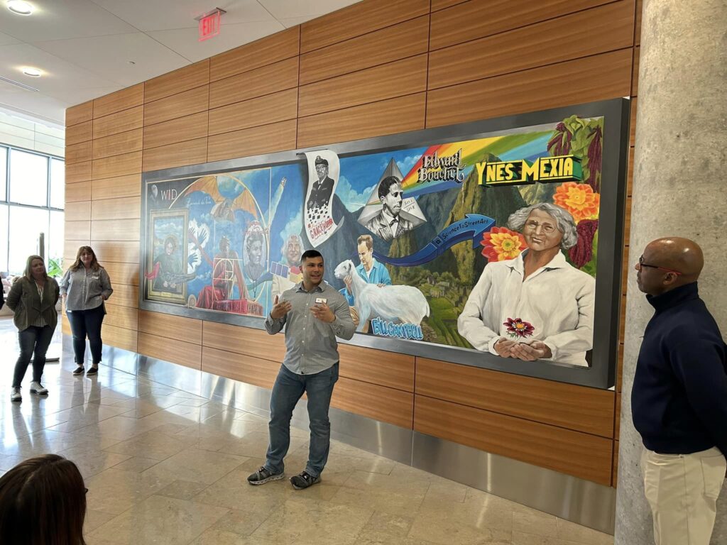 A man stands in front of a colorful mural celebrating Latino culture.