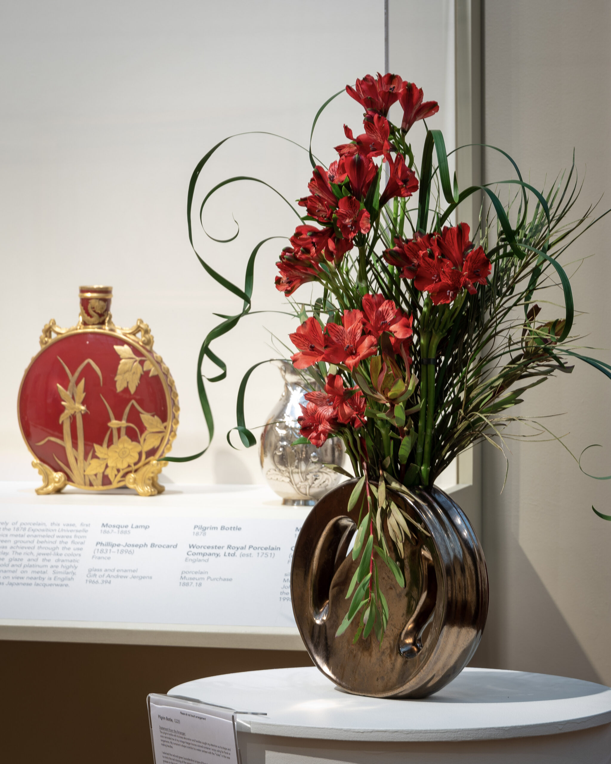 A red and gold porcelain bottle with a pattern of leaves on it, and a red and gold flower arrangement