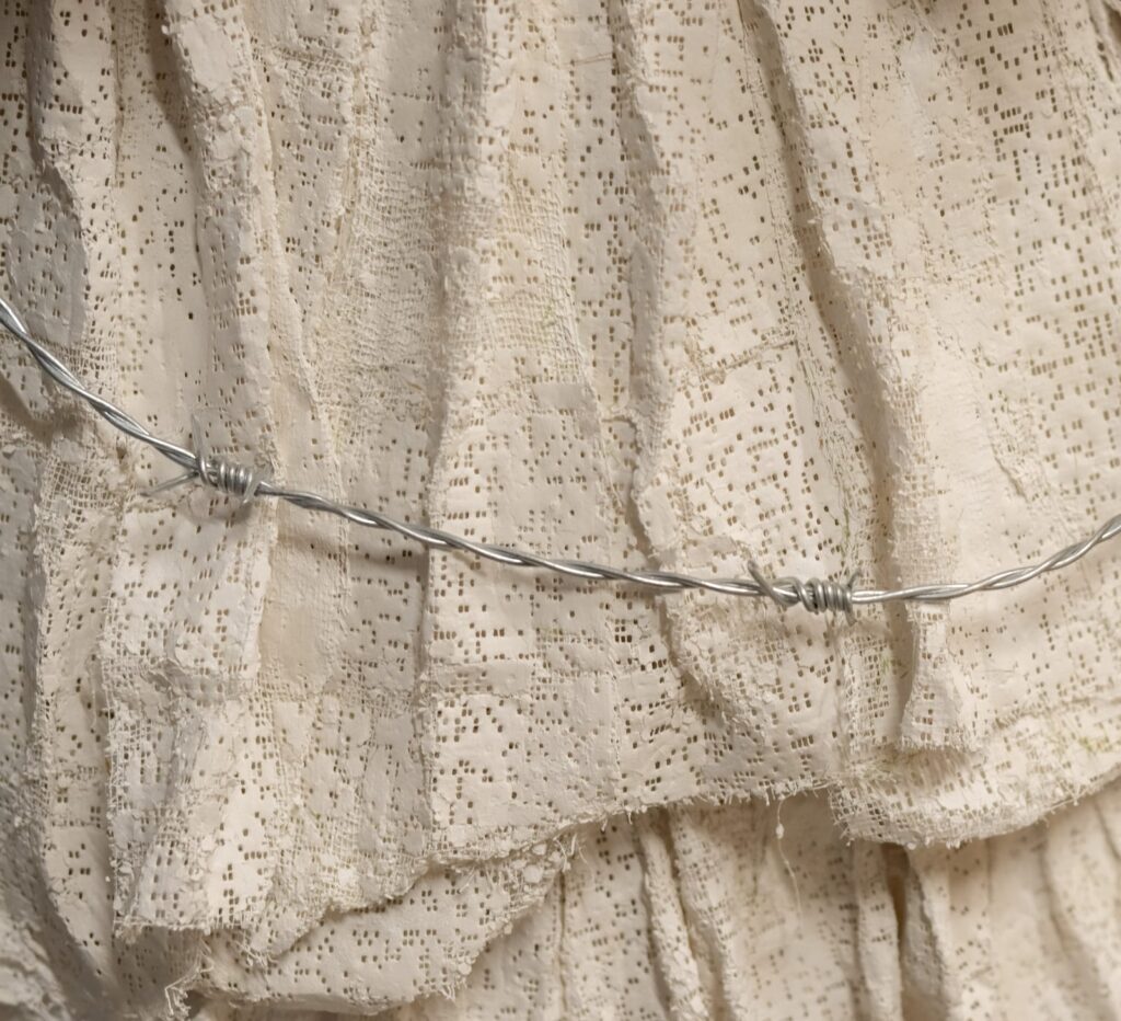 White fabric with holes in it and a thin barbed wire metal string running through it.