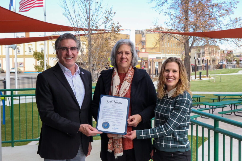 Three people hold up a proclamation on a beautiful outdoor patio