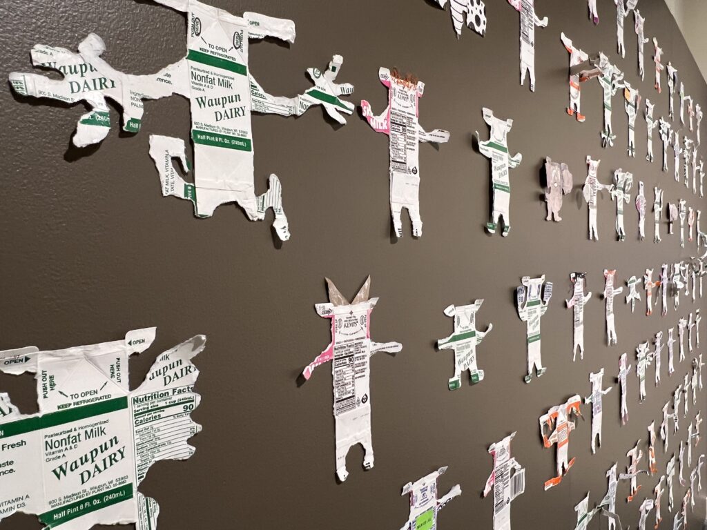 A wall with abstract figures made with torn milk and juice cartons.