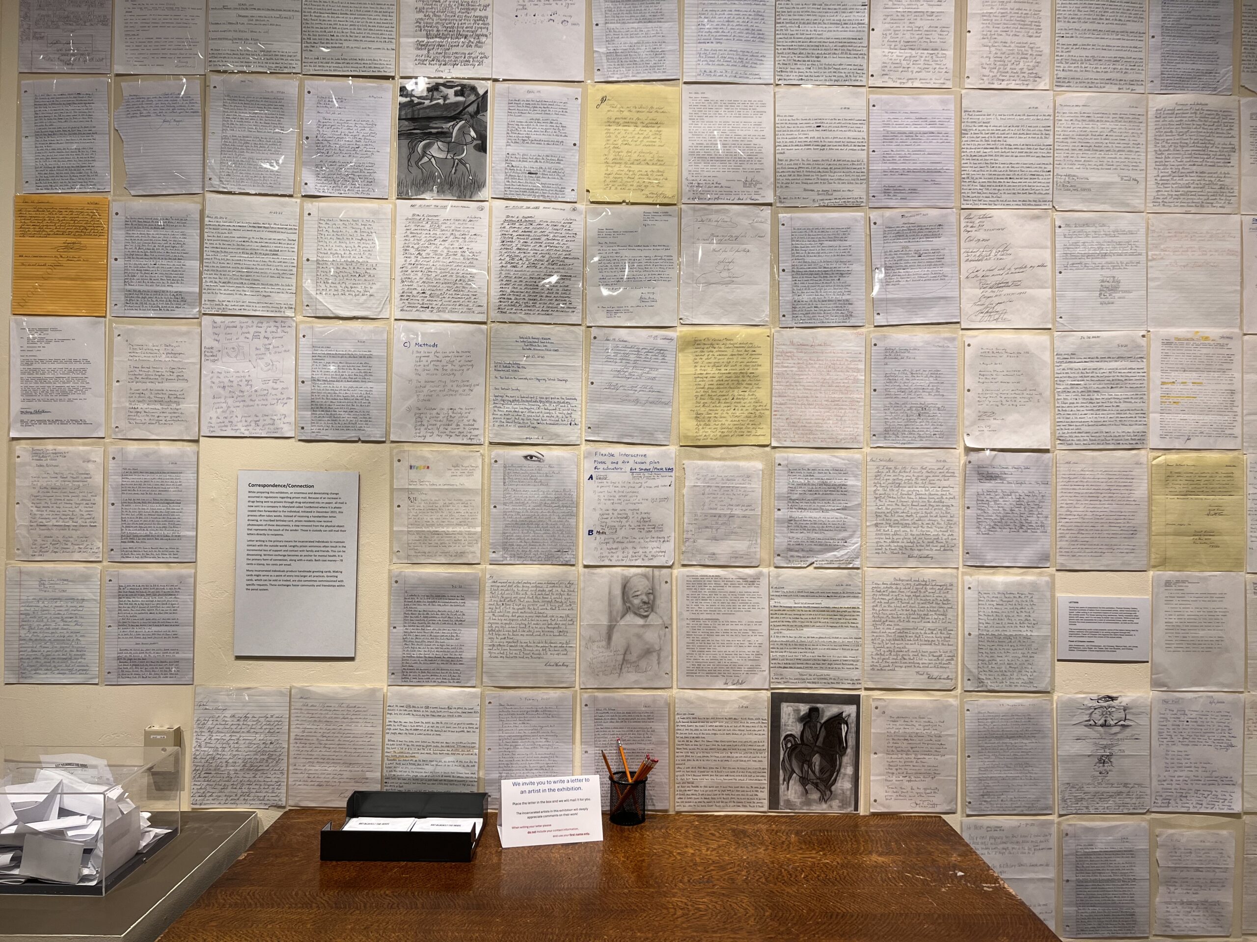 A wall covered with handwritten letters. There's a table by the wall with paper and pencils.
