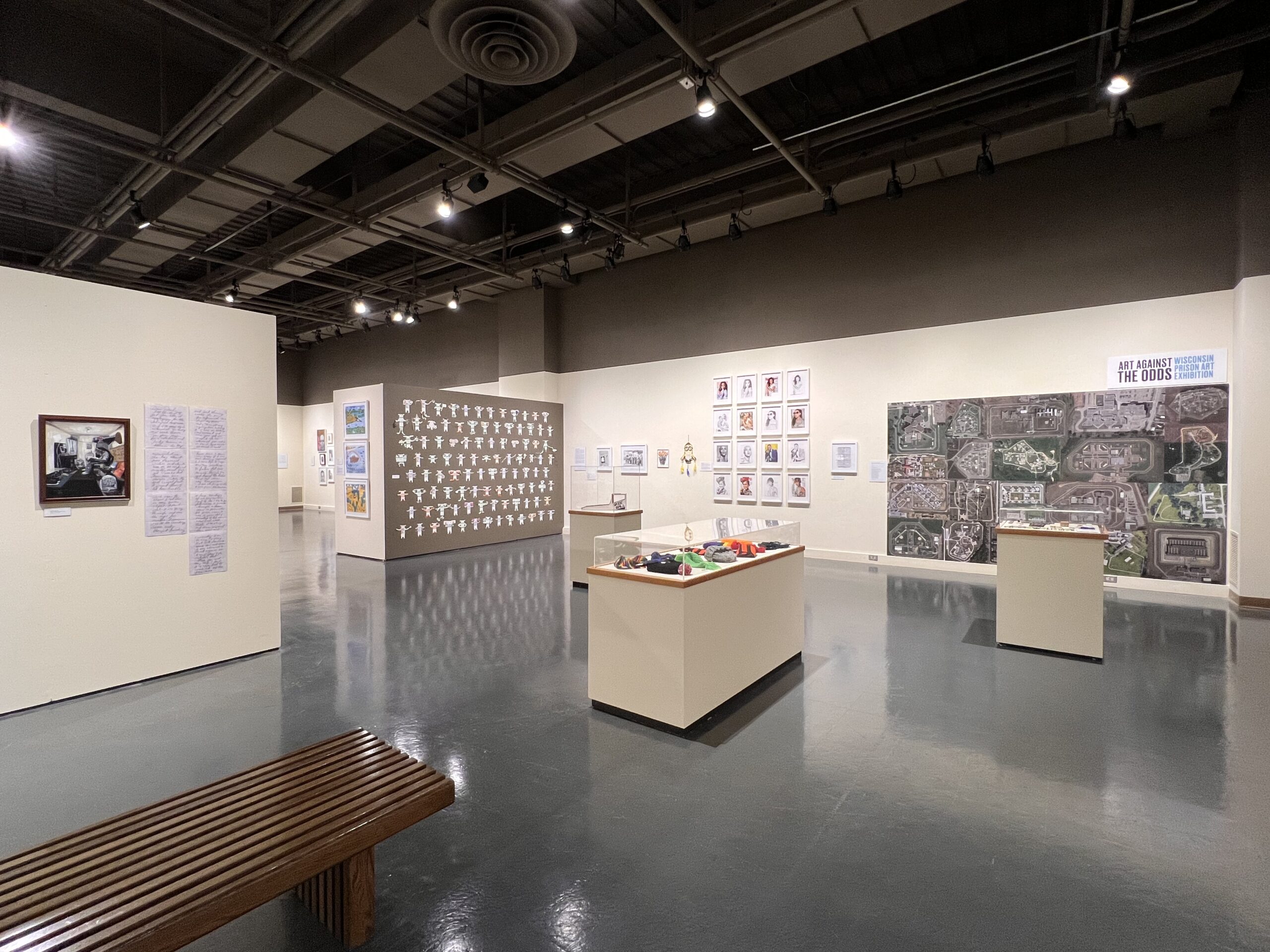 A wide view of an art exhibition with displays of objects and walls with hung artworks.