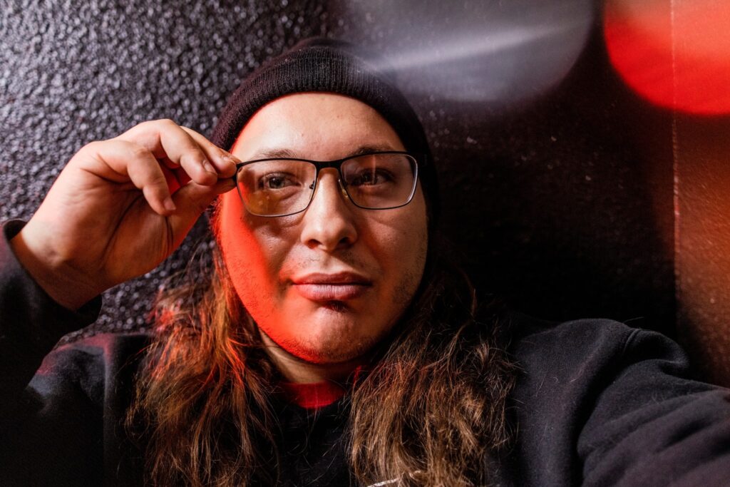 A person of medium skin tone with long hair wearing a beanie and glasses.