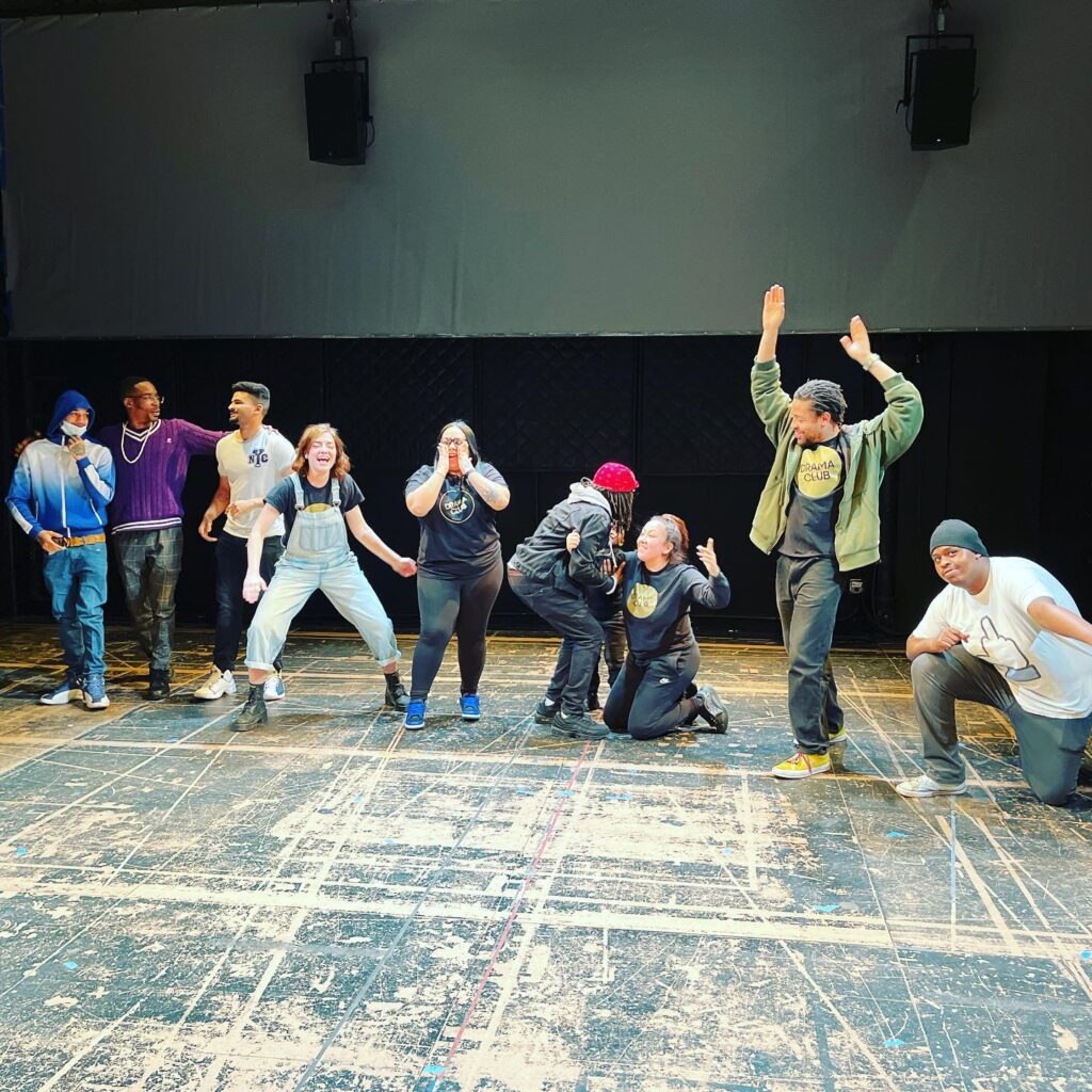 A group of nine people dynamically pose on a stage
