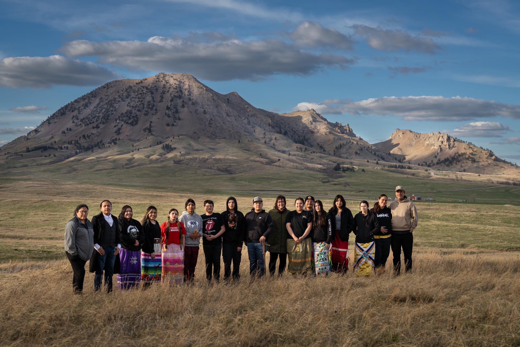 A group of Native youth and elders stand in front of a beautiful butte.