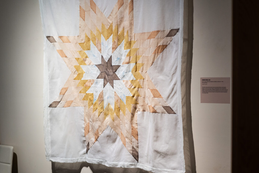 A large quilt featuring a multicolored star design, hung on the wall.