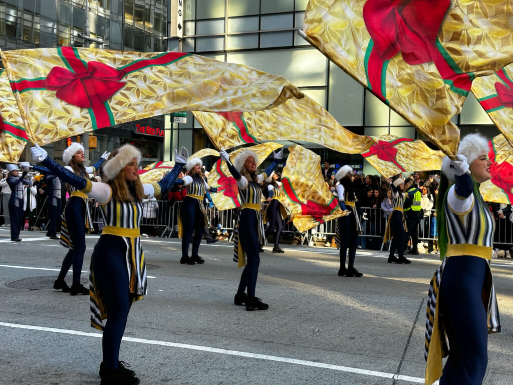 Young adults performing with flags and in costume at a street parade.