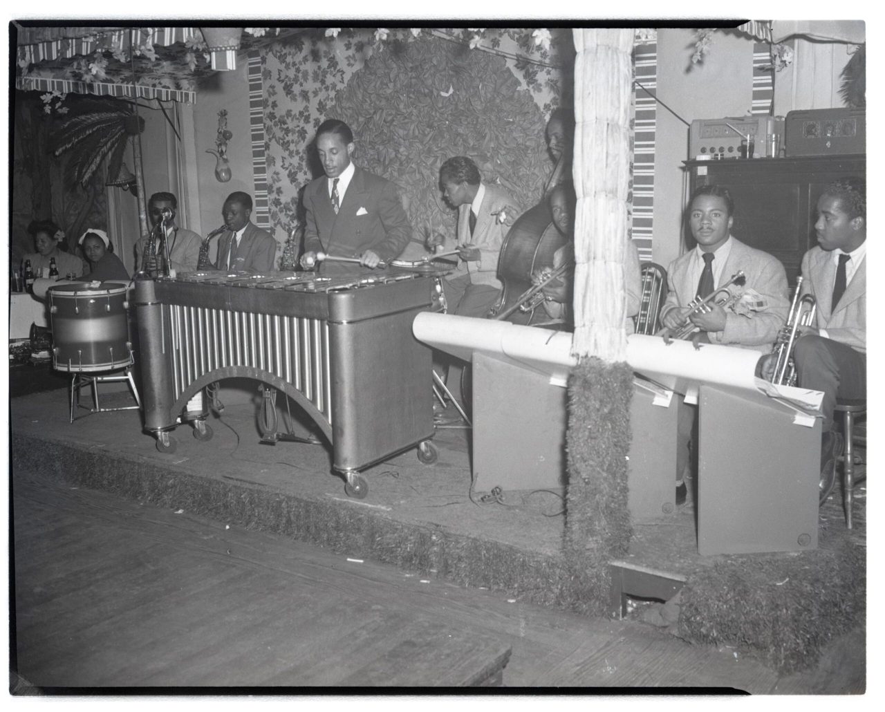 An archival black and white photo of an all-Black band on stage with the musicians playing different instruments.