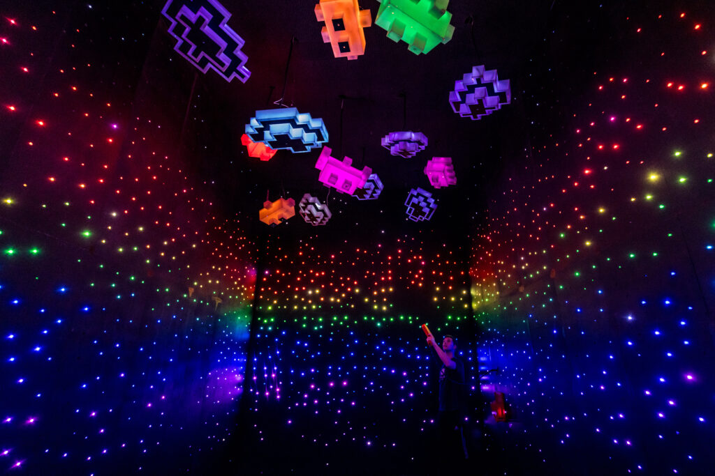 A dark room lit by small brightly colored lights and Lego-like light fixtures hanging from the ceiling.