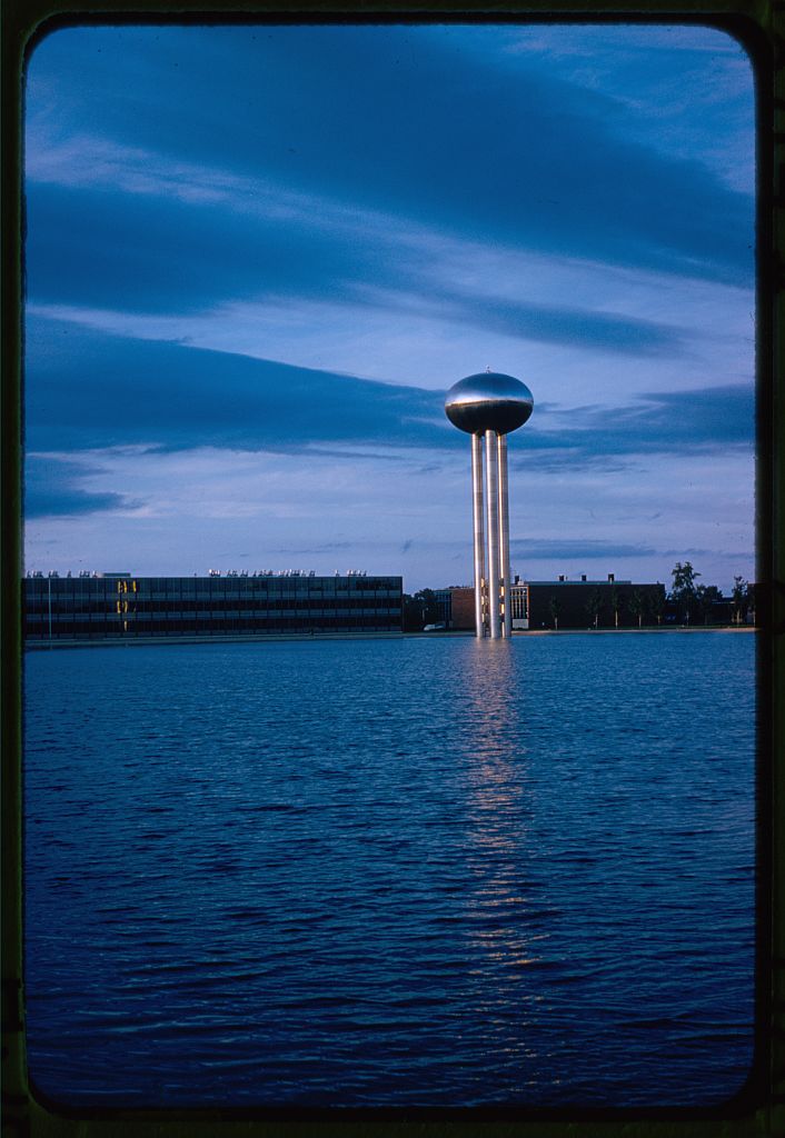 A tall metallic water tower stands in the distance, at the edge of a water body.