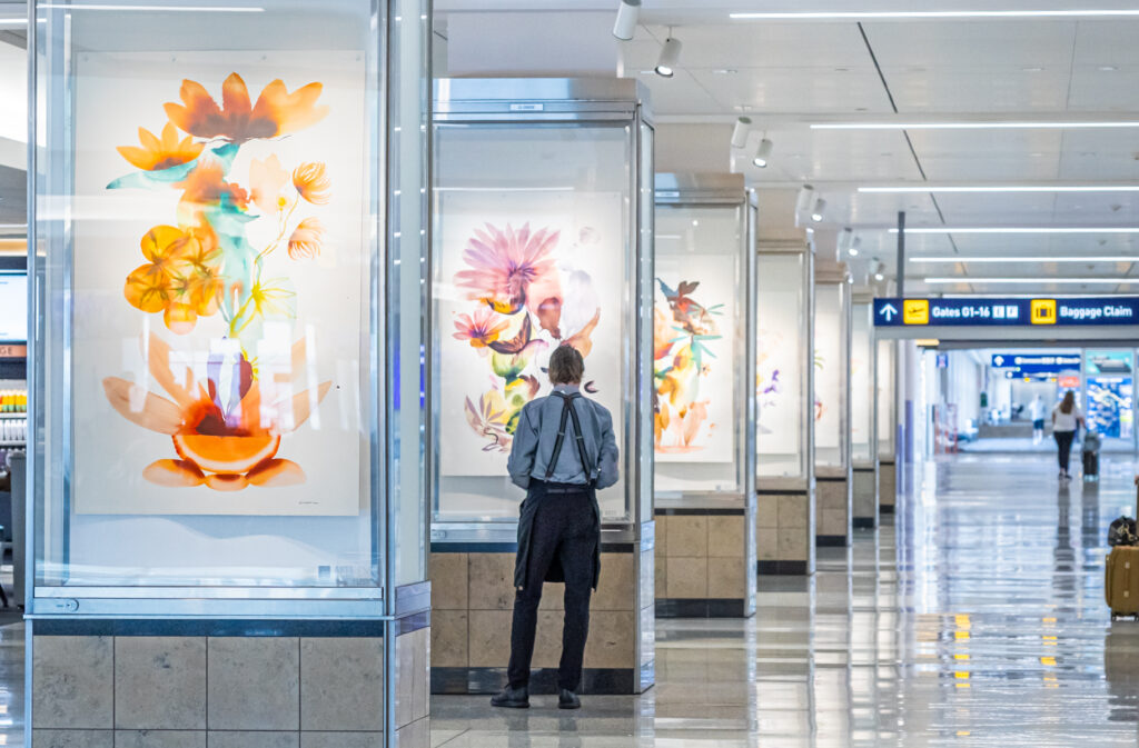 A person stands by a tall glass display with floral watercolor paintings.