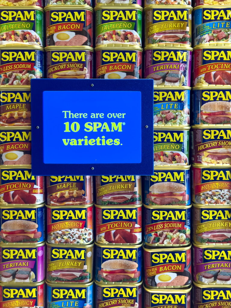 A wall of SPAM cans of various flavors, with a sign reading, "There are over 10 SPAM varieties."