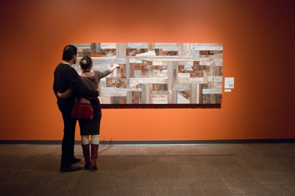 A man and woman look at a beautiful geometric abstract art piece on an orange wall