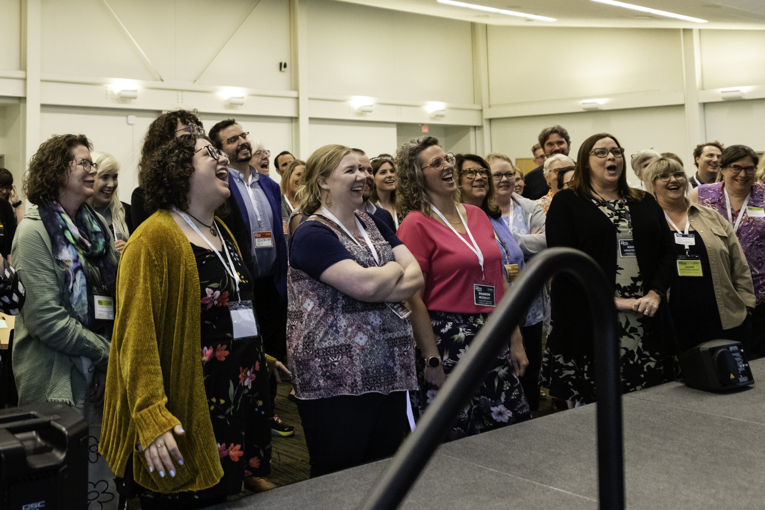 A group of arts administrators wearing lanyards look at a stage with excited faces