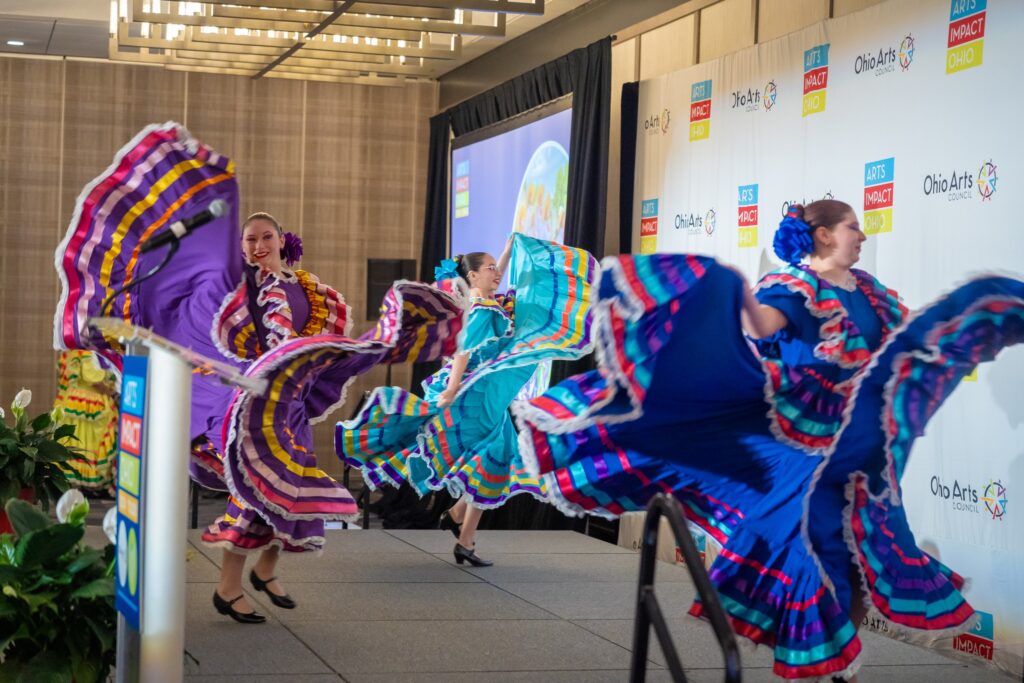 Three dancers in traditional mexican Folklórico dresses dance on stage