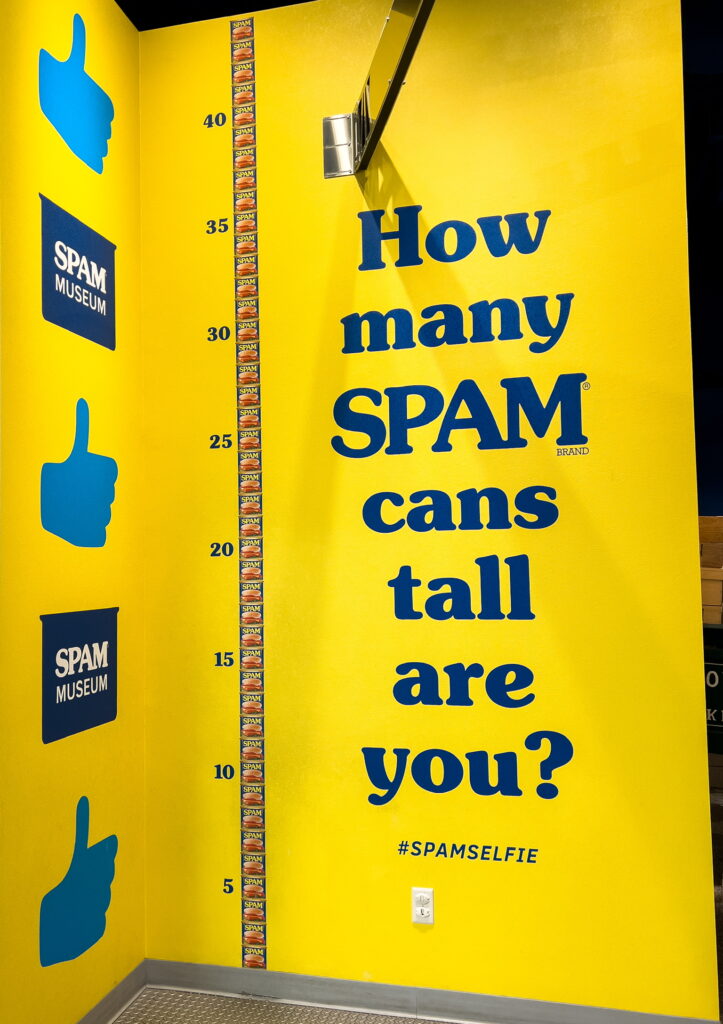 A photo op with images of SPAM cans stacked on top of one another, with large text reading, "How many SPAM cans tall are you?"