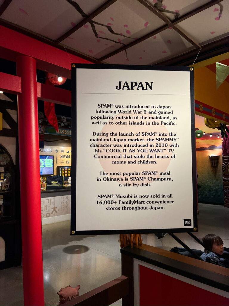 A sign reading, “SPAM was introduced to Japan following World War 2 and gained popularity outside of the mainland, as well as to other islands in the Pacific. During the launch of SPAM into the mainland Japan market, the SPAMMY character was introduced in 2010 with his "COOK IT AS YOU WANT" TV Commercial that stole the hearts of moms and children. The most popular SPAM meal in Okinawa is SPAM Champuru, a stir fry dish. SPAM Musubi is now sold in all 16,000+ FamilyMart convenience stores throughout Japan.”