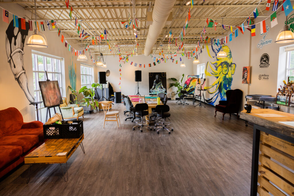 A large room with a long table and chairs around it. There are small paper flags of different countries hanging all across the ceiling of the room. There are murals and paintings on the walls of the room.