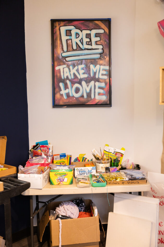 A table of different art supples with a large sign that reads "Free" and "take me home"