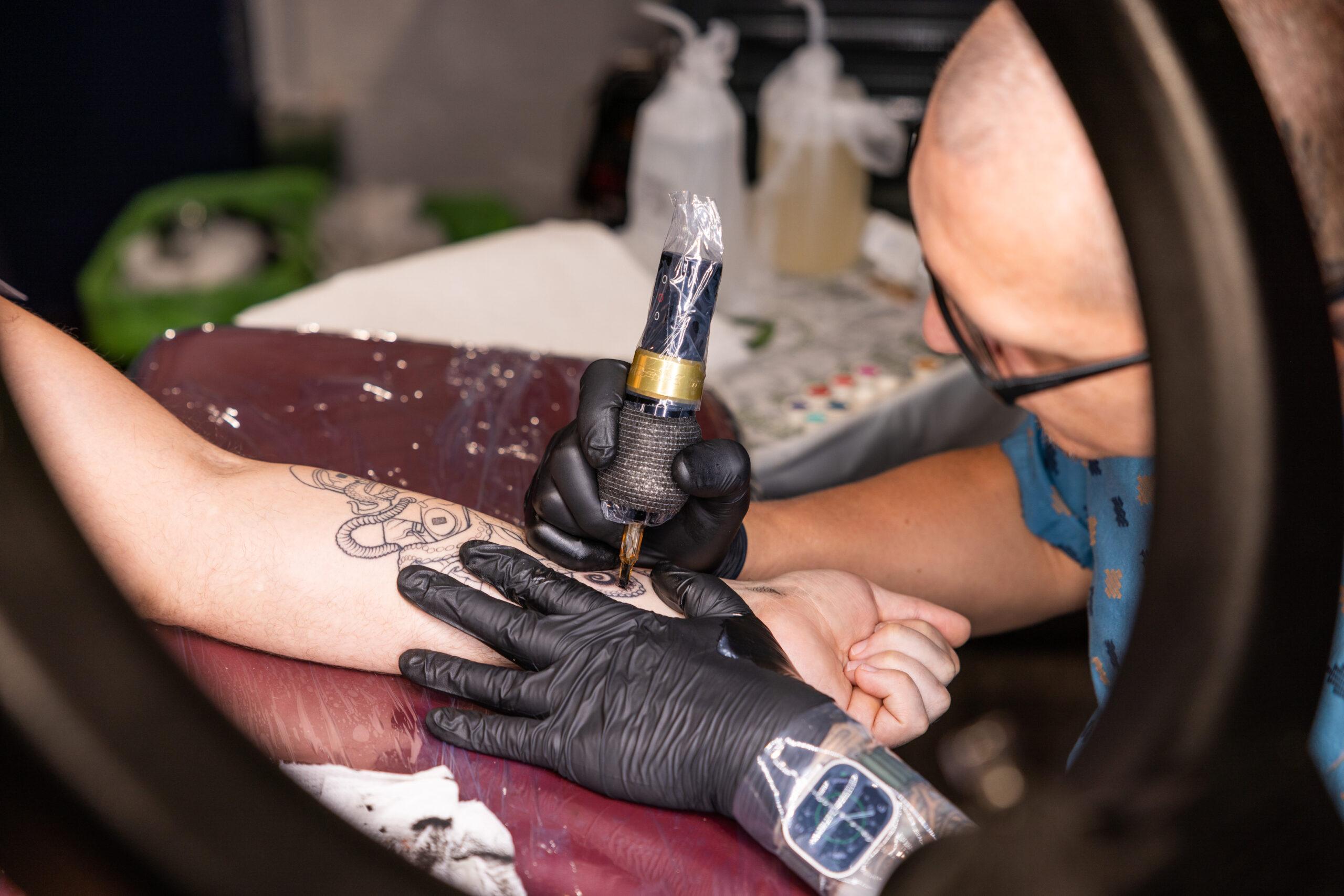 A person holding a tattoo gun as they draw on a person's forearm.