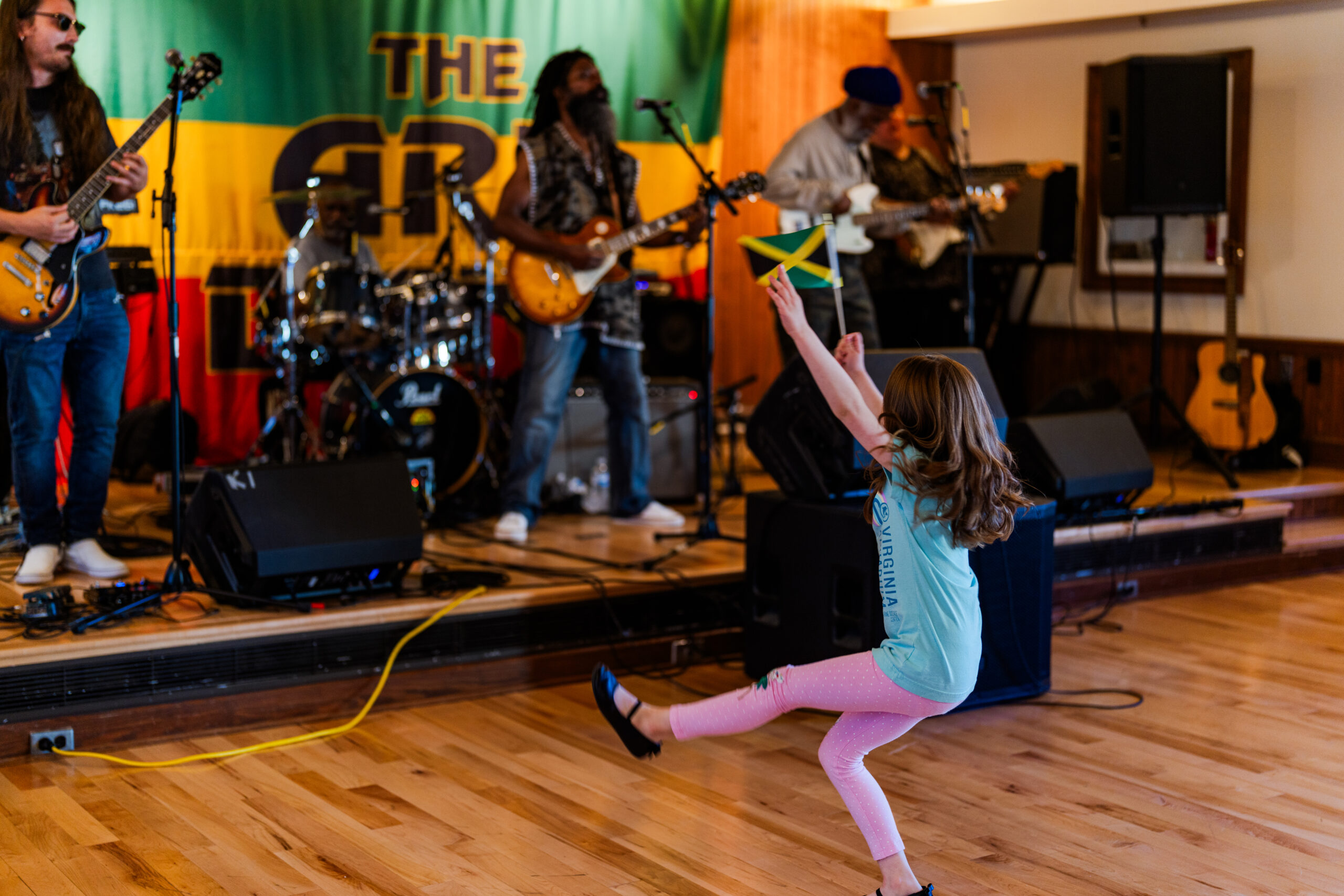 A young girl dancing in front of a stage where a band performs in front of a large banner reading, "The Ark Band."