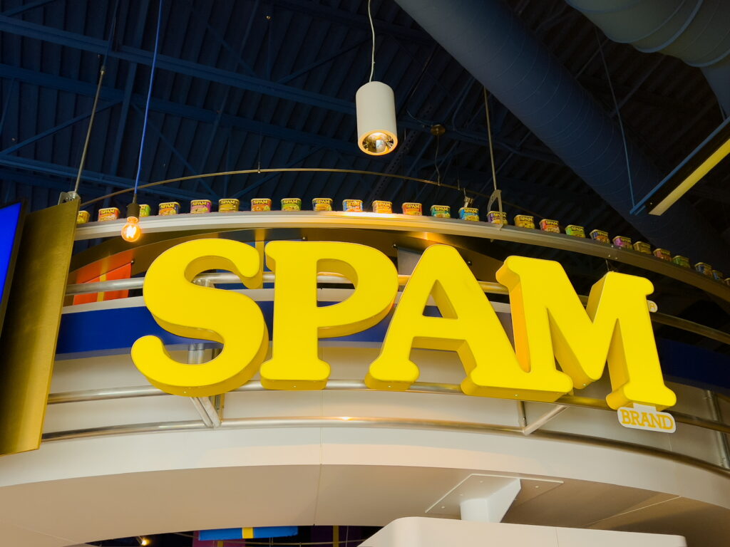 A large yellow sign reading, "SPAM brand," with a conveyor belt of SPAM cans above it.