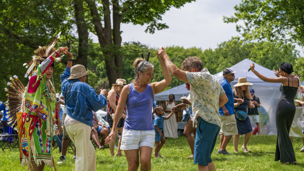 People in Native regalia dance with people in summery outfits