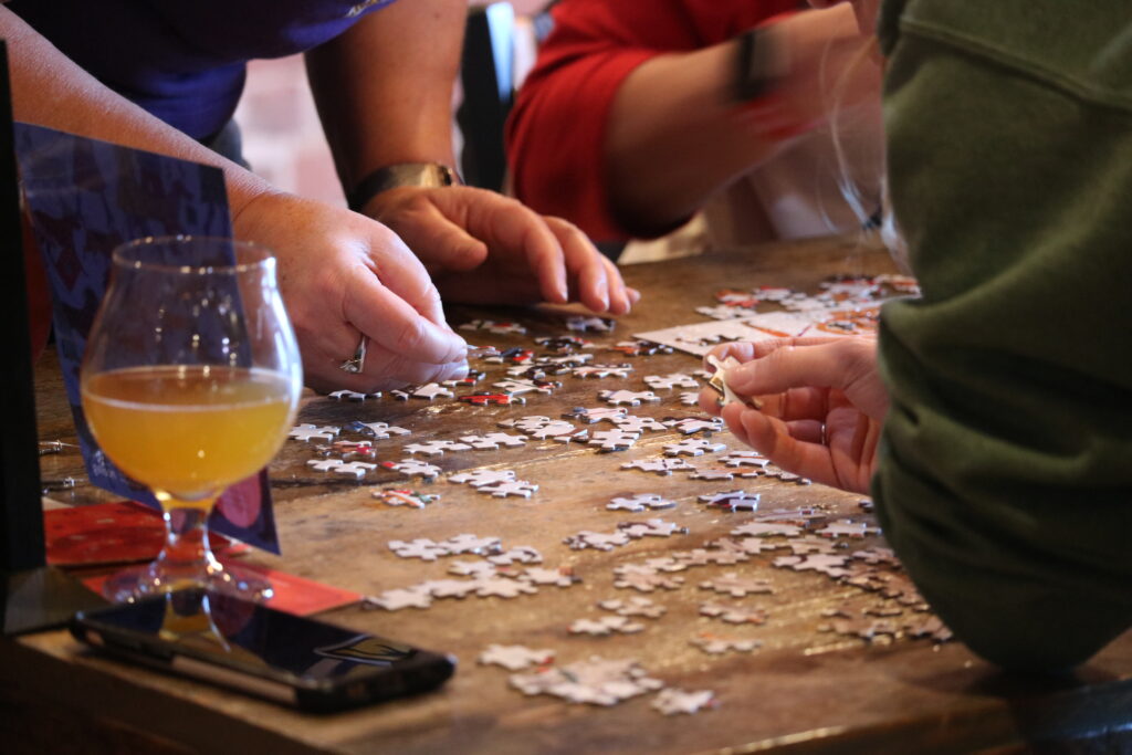 A close up of hands working on a jigsaw puzzle on a table.