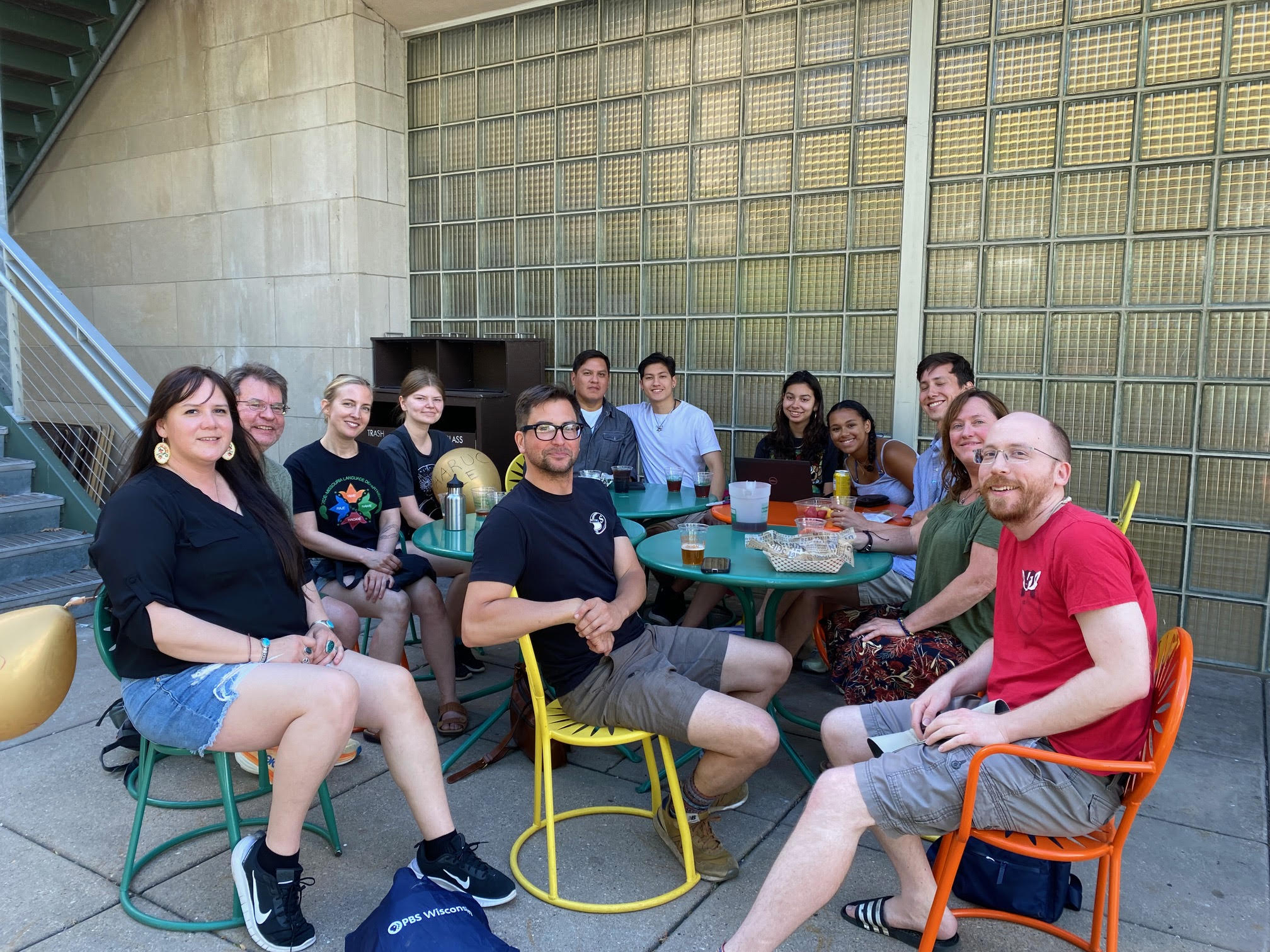 A group of people sit around tables and smile as they all face on direction. There are cups with beverages on the tables.