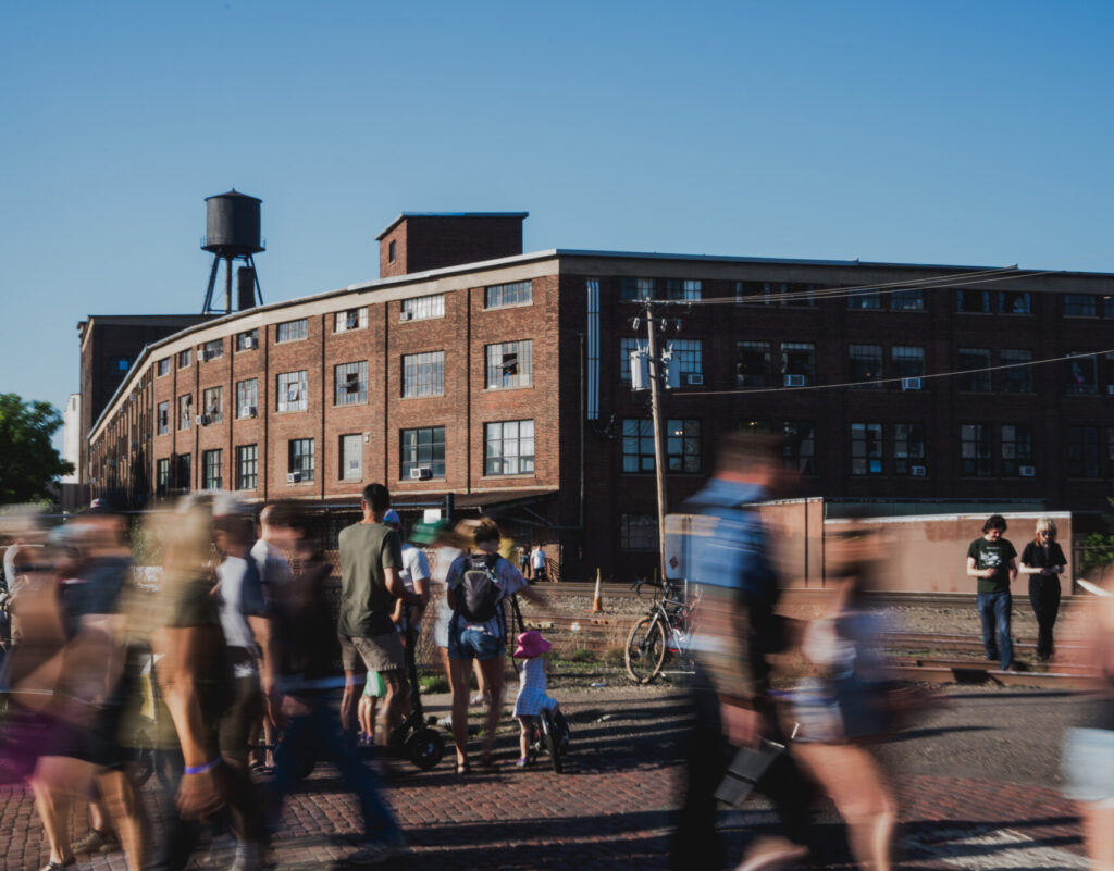 People walking on a brick paved street with a large brick building in the background.