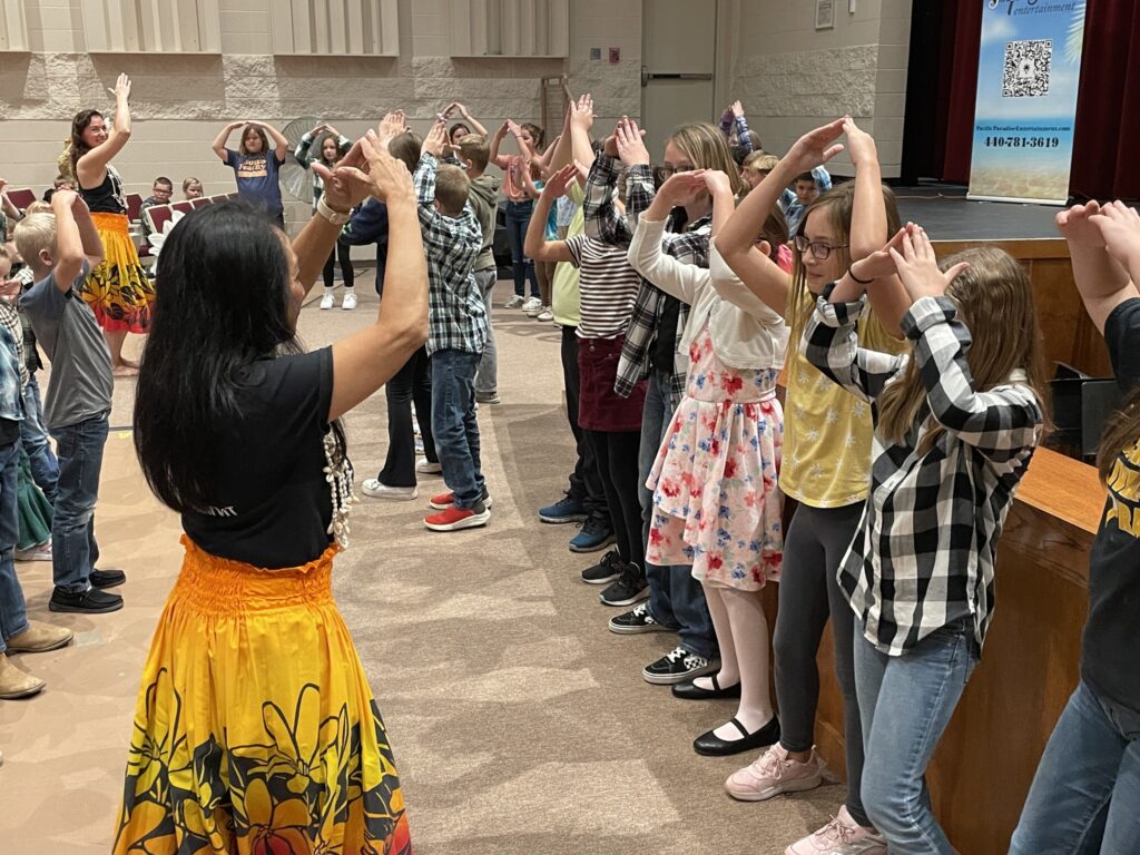 A group of youth and dancers in front of a stage, learning a dance.