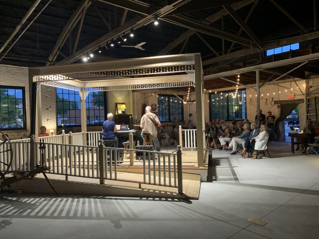 An audience in a speakeasy-decorated space watching two musicians perform on a small stage.