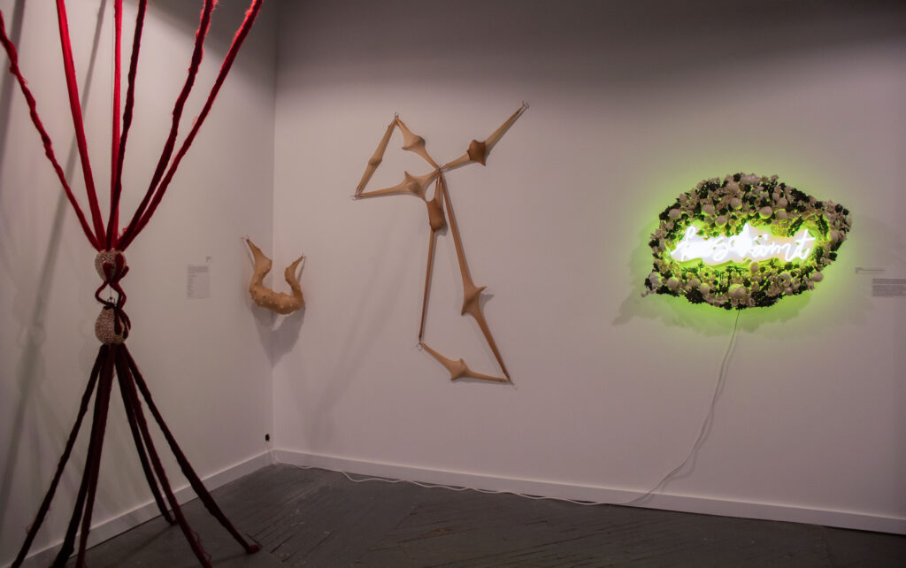 A gallery filled with angular sculptures made out of clay and felt and a neon sign