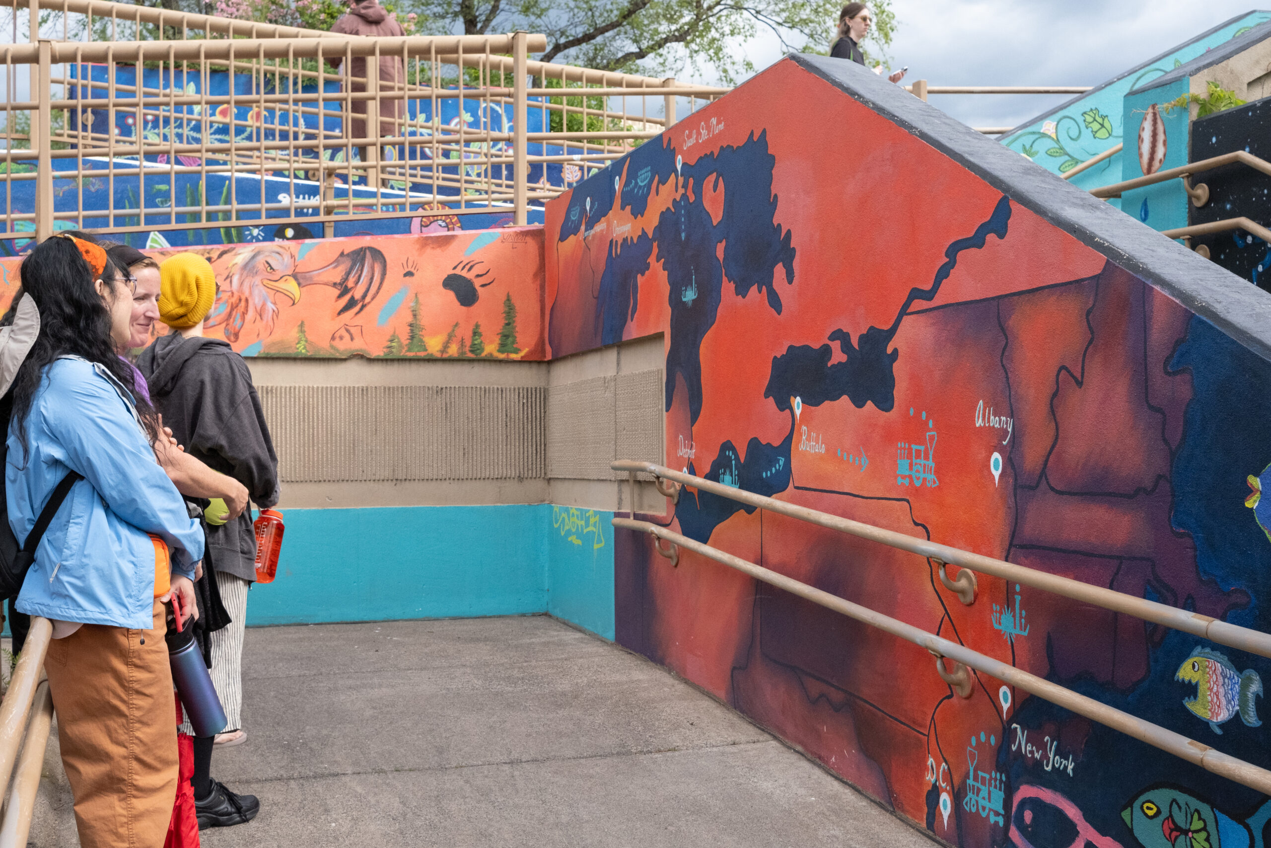 People stand across from a wall with a mural depicting a map.