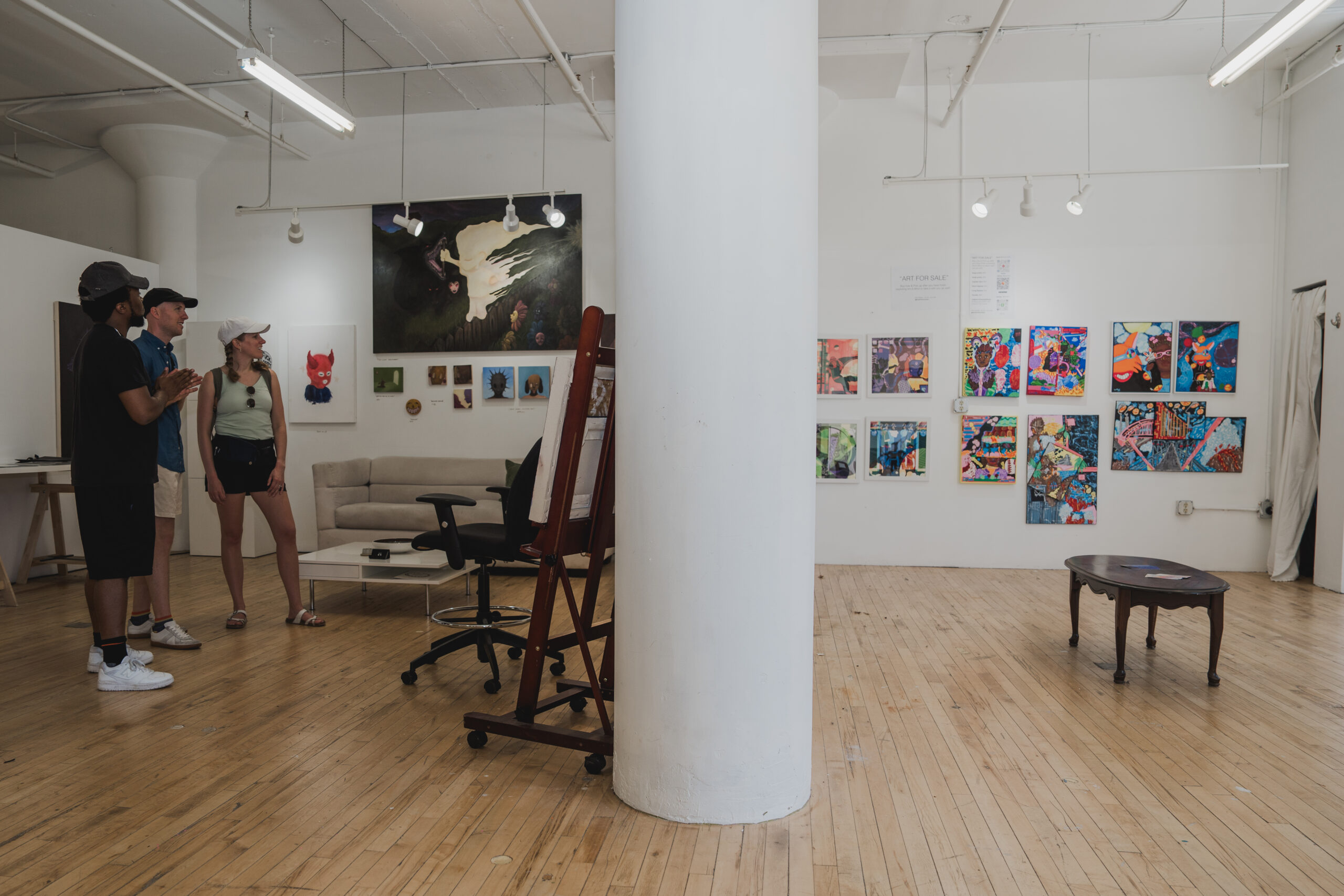 Three people standing close to each other looking in one direction. The walls around them have different paintings of varying sizes.