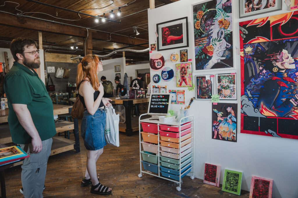 Two people stand next to a white wall and look at the different artworks mounted on the wall.