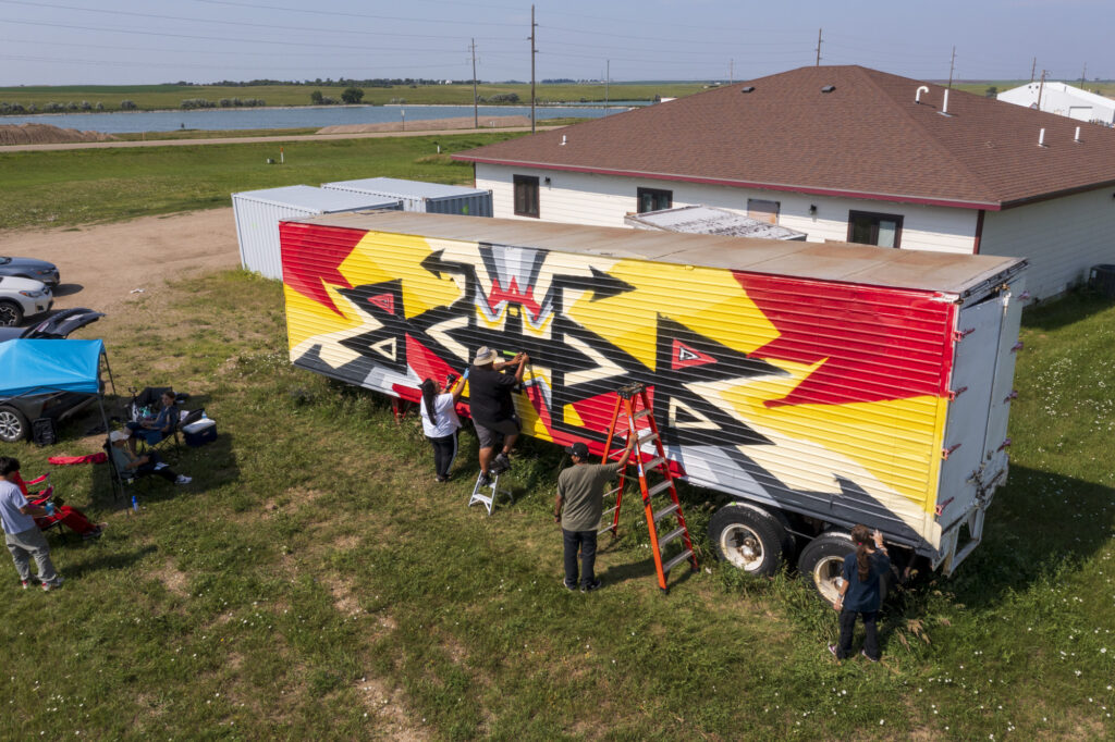 An aerial view of three people painting a shipping container.