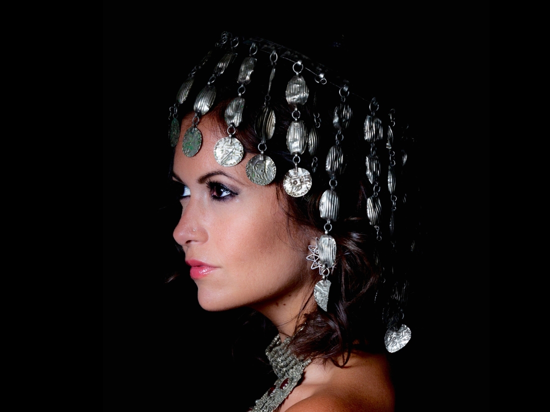 A person with medium light skin tone wearing a large silver necklace and a silver coin headpiece