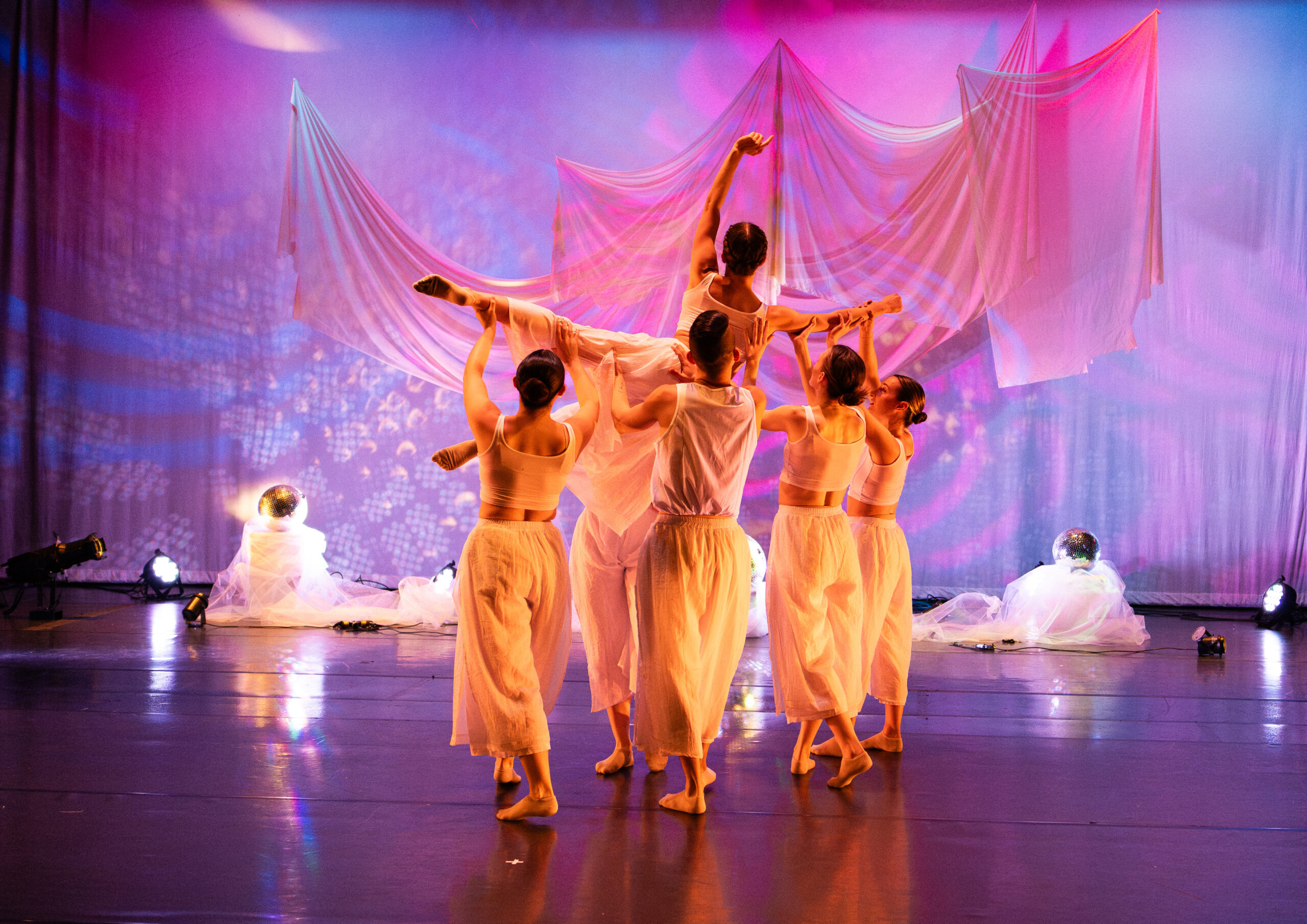 Five dancers on stage with four lifting up one.