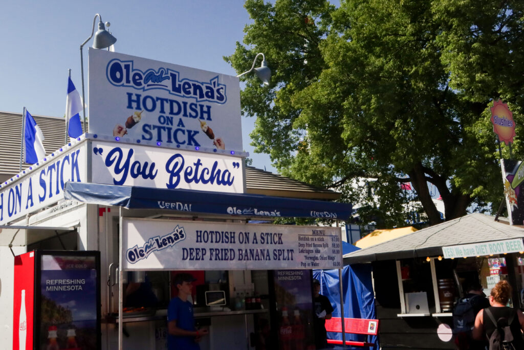 A fair food booth with signage reading "Ole Lena's Hotdish on a Stick."