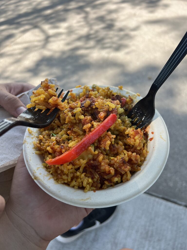 A paper bowl of yellow rice with vegetables and two forks.