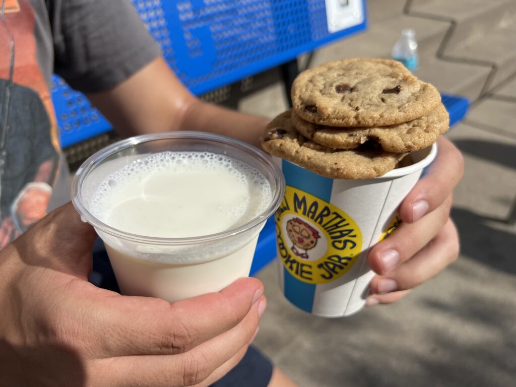 Two hands holding a cup of milk and a cup of cookies with the Sweet Martha's logo.