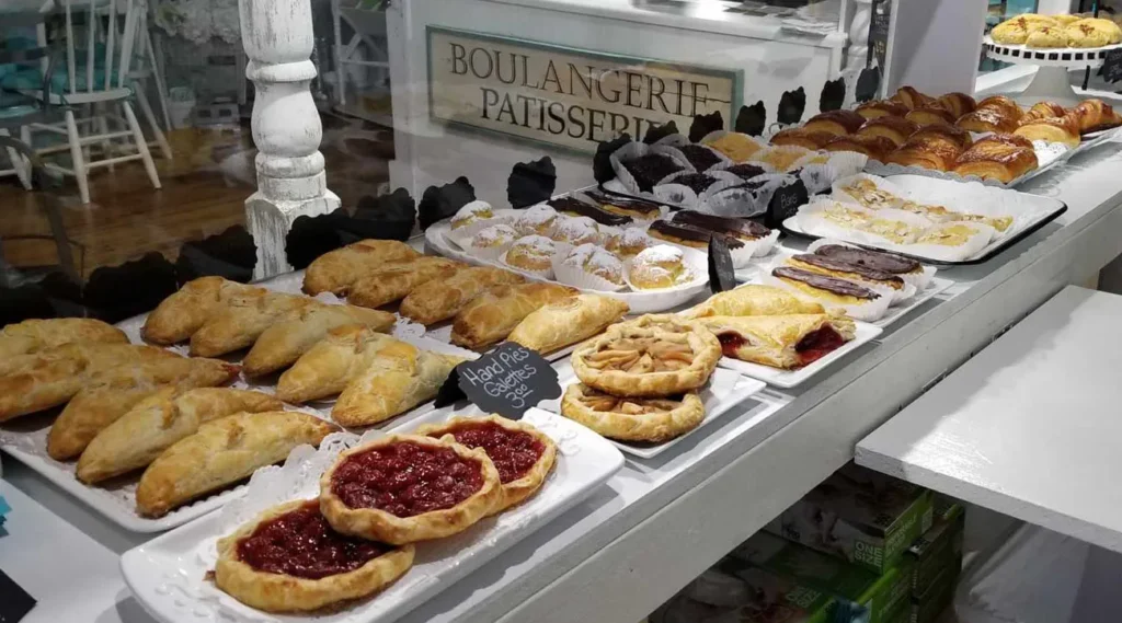 Two rows of pastries on trays sit behind a class window on a white counter. There are hand pies and galettes for $3. There are also Éclairs, croissants, and turnovers.