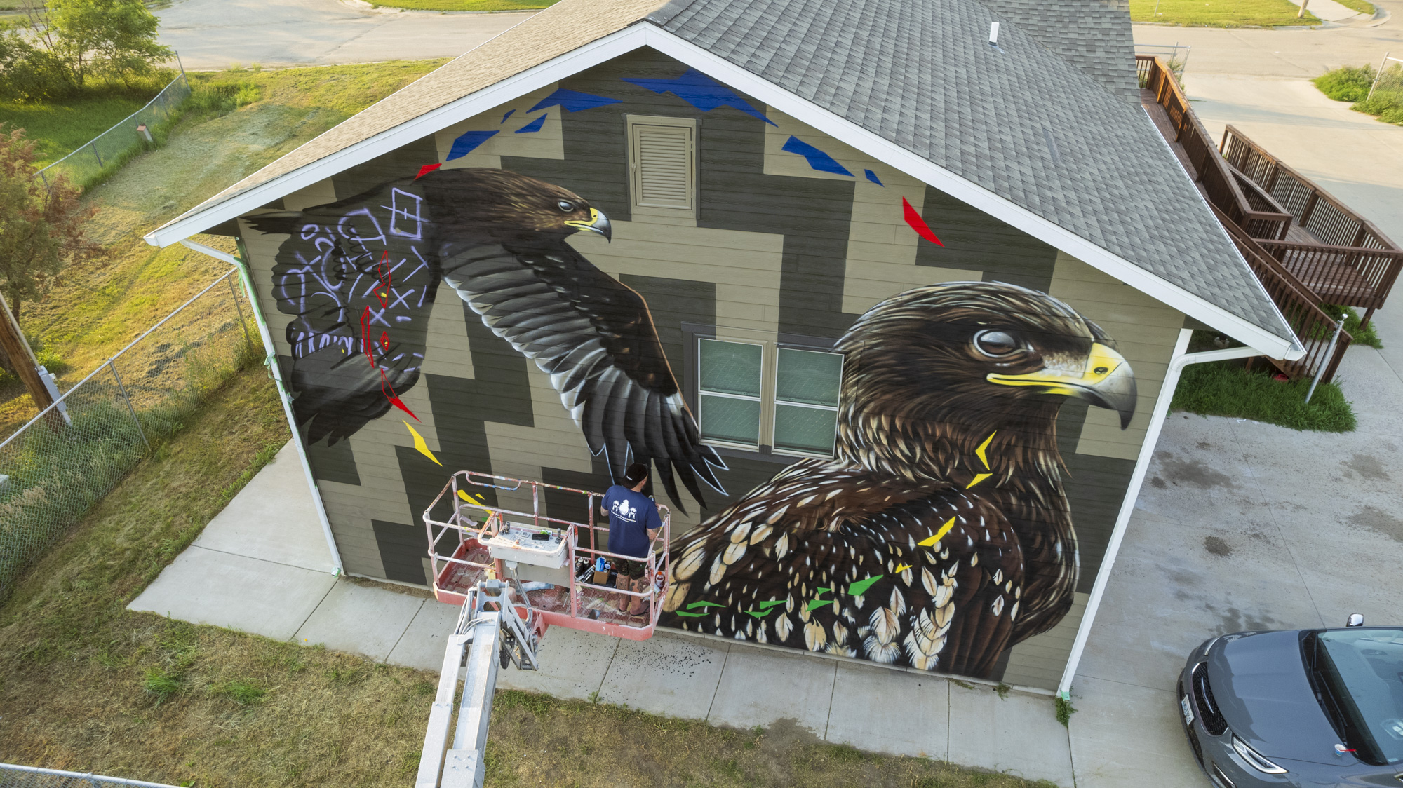 A mural in progress on a side of a building. It depicts two large birds, one in flight and the other resting.