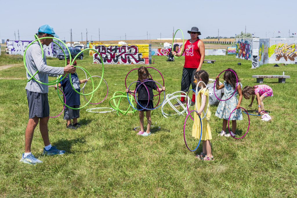 Two adults teaching young children a traditional dance that uses hoops. The children are all holding multiple hoops in their hands.