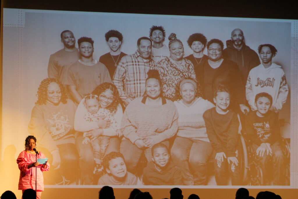 A person stands in front of a projected image of an extended family.