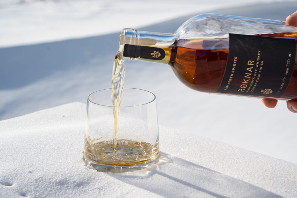 A hand pouring whiskey from a bottle into a small glass.